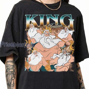 May include: Black t-shirt featuring a graphic of King Triton from The Little Mermaid. The design includes the text "KING Triton" in a vintage style, with multiple illustrations of the character. The shirt has a crew neck and short sleeves.