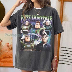 May include: Dark gray Buzz Lightyear graphic t-shirt. The shirt features a colorful graphic of Buzz Lightyear and the text "Buzz Lightyear" in a green and purple font. The shirt is a relaxed fit.