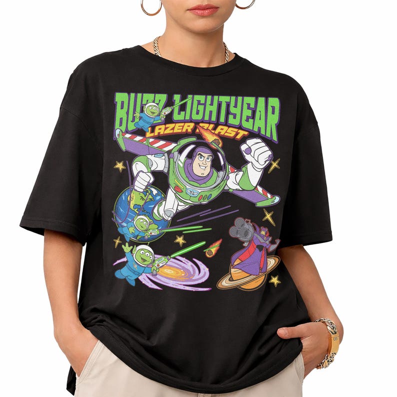 May include: Black t-shirt featuring a graphic of Buzz Lightyear in a space scene with the text "Buzz Lightyear Lazer Blast" in green and white. The design includes cartoon characters, planets, and stars.