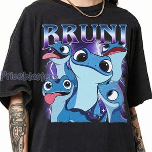 May include: Dark gray t-shirt featuring a graphic of several blue salamanders with the word "BRUNI" in a purple and white font. The salamanders have large eyes and are set against a purple lightning background.