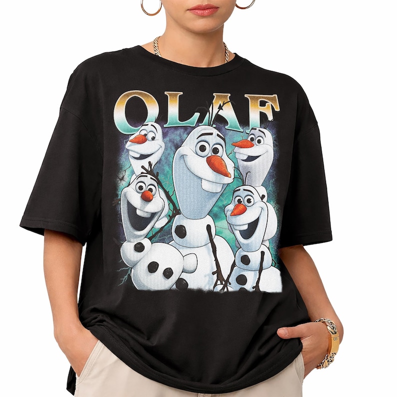 Puede incluir: Camiseta negra con un gr&aacute;fico de Olaf de Frozen. El dise&ntilde;o presenta varios personajes de Olaf con narices de zanahoria y caras sonrientes. La palabra "OLAF" est&aacute; impresa en la parte superior en una fuente estilizada.