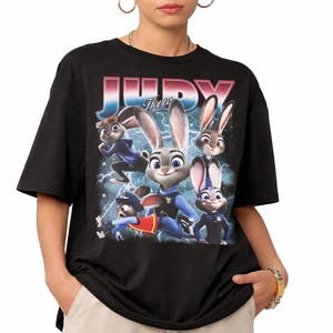 Op de afbeelding: Zwart t-shirt met een afbeelding van Judy Hopps uit Zootopia. Het ontwerp bevat de naam "JUDY" in een retro lettertype, met afbeeldingen van Judy in verschillende poses tegen een achtergrond van bliksem. Het shirt heeft korte mouwen en een ronde hals.