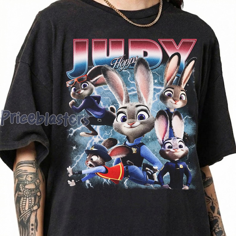 Op de afbeelding: Donkergrijze t-shirt met een kleurrijke afbeelding van Judy Hopps en andere personages uit Zootopia. Het woord "JUDY" staat in grote, gestileerde letters boven de personages. Het shirt heeft een ronde hals en korte mouwen.