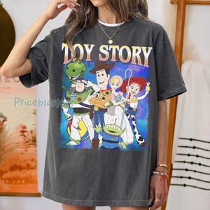Puede incluir: Camiseta gris oscuro con las palabras "TOY STORY" en naranja y amarillo. El gr&aacute;fico presenta personajes animados, incluyendo a Woody, Buzz Lightyear y otros personajes de la pel&iacute;cula.