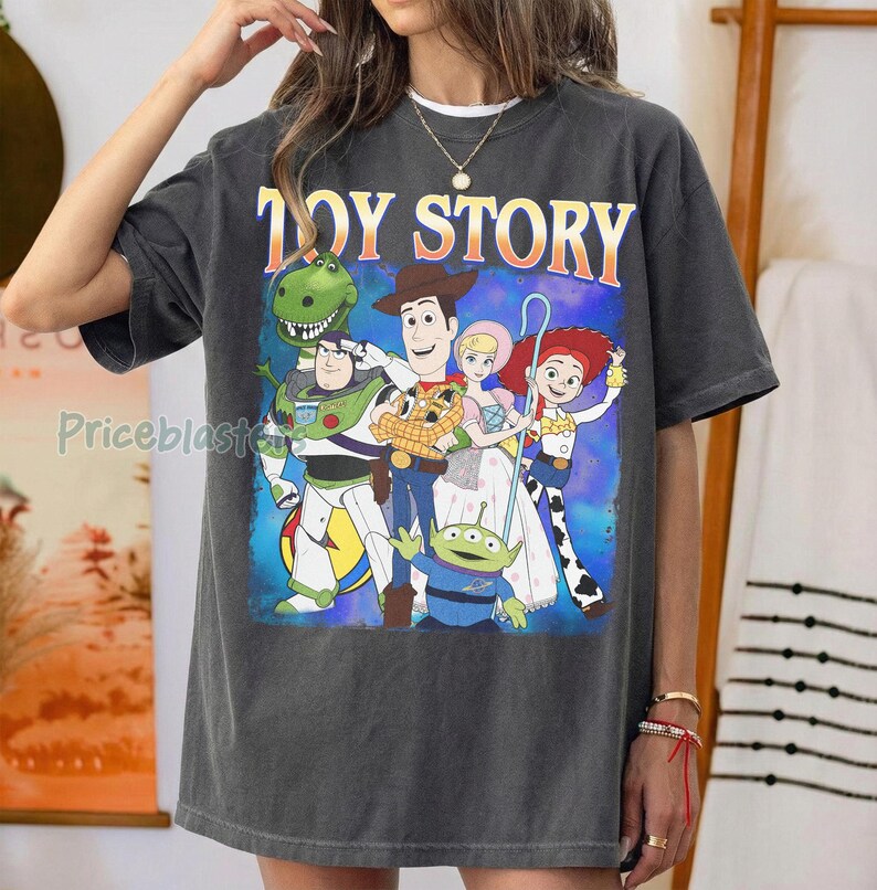 Puede incluir: Camiseta gris oscuro con las palabras "TOY STORY" en naranja y amarillo. El gr&aacute;fico presenta personajes animados, incluyendo a Woody, Buzz Lightyear y otros personajes de la pel&iacute;cula.
