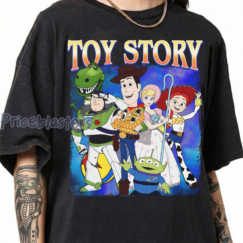 Puede incluir: Camiseta gris oscuro con un gr&aacute;fico colorido de los personajes de Toy Story, incluyendo a Woody y Buzz Lightyear. Las palabras "TOY STORY" est&aacute;n impresas en naranja sobre los personajes. El dise&ntilde;o est&aacute; sobre un fondo azul.