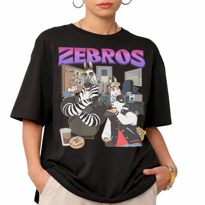 Pu&ograve; includere: T-shirt nero con un'illustrazione a cartoni animati di due zebre in un ambiente di stazione di polizia, con la scritta "ZEBROS" in viola e rosa. Una zebra indossa una giacca, l'altra &egrave; seduta. Una tazza di caff&egrave; e una ciambella in primo piano.
