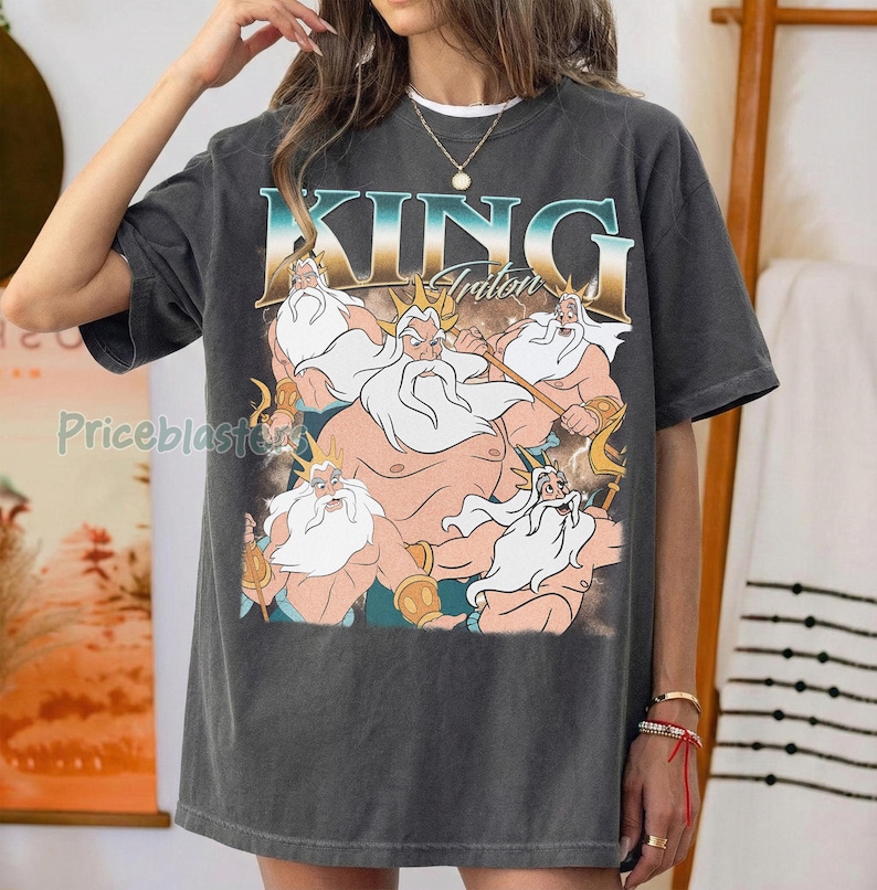May include: Dark gray t-shirt featuring a graphic of King Triton with a trident. The text "KING Triton" is displayed above the illustration in a teal and gold font. The shirt has a vintage, worn look.