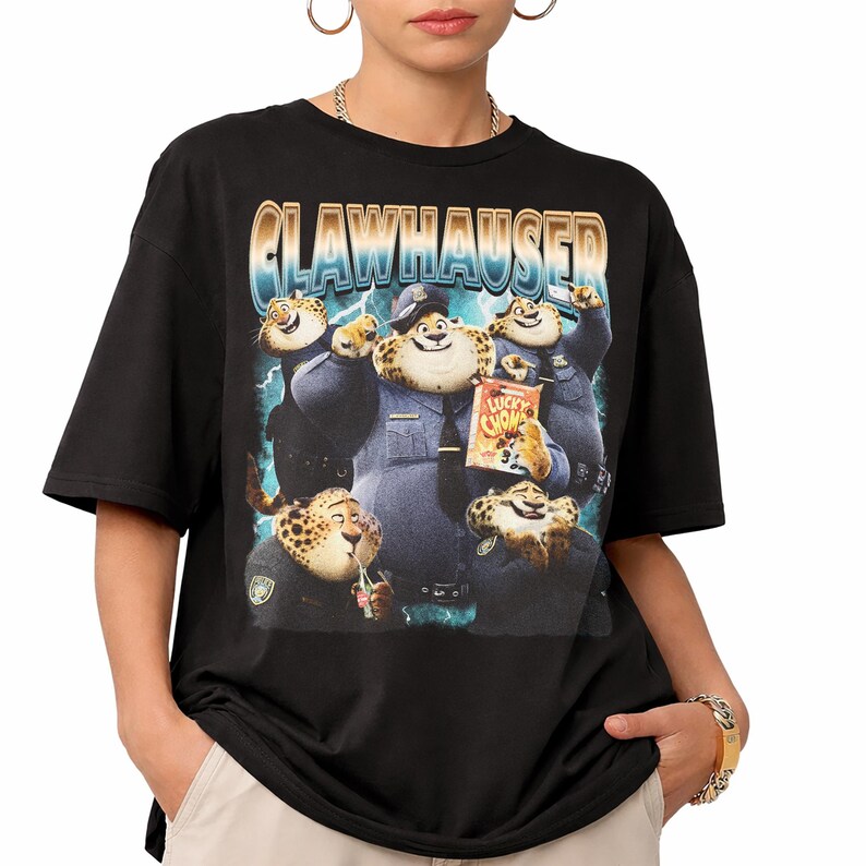 Puede incluir: Camiseta negra con un gr&aacute;fico de Clawhauser de Zootopia. El dise&ntilde;o incluye el texto "CLAWHAUSER" en una fuente retro e im&aacute;genes de Clawhauser con uniforme de polic&iacute;a, sosteniendo bocadillos. La camiseta es de cuello redondo y manga corta.