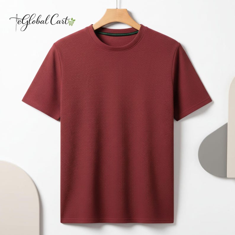 May include: A short-sleeved, burgundy t-shirt with a ribbed texture, hanging on a wooden hanger. The shirt has a crew neck with a green trim. The Global Cart logo is visible in the top left corner.