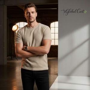 May include: A man wearing a beige short-sleeved textured t-shirt and black jeans, arms crossed. He is wearing a watch. The background includes windows, a light, and a wall with the text "eGlobal Cart".