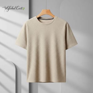 May include: A short-sleeved, beige t-shirt with a textured, ribbed design. The shirt has a crew neck with a dark trim and is hanging on a wooden hanger. The Global Cart logo is visible in the upper left corner.