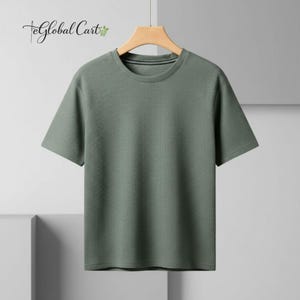 May include: A short-sleeved, sage green t-shirt with a textured, waffle-like pattern. The shirt has a crew neck and is hanging on a wooden hanger. The brand name "eGlobal Cart" is visible in the upper left corner.