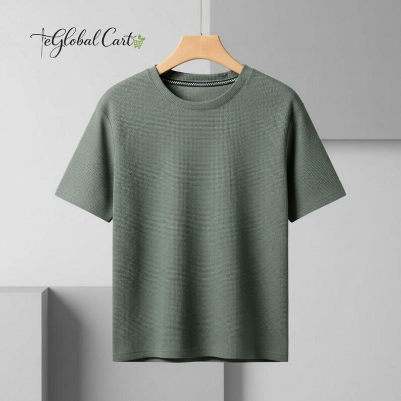 May include: A short-sleeved, sage green t-shirt with a textured, waffle-like pattern. The shirt has a crew neck and is hanging on a wooden hanger. The brand name "eGlobal Cart" is visible in the upper left corner.
