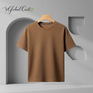 May include: A short-sleeved, brown t-shirt hangs from a wooden hanger. The shirt has a textured pattern and a crew neck with a thin, dark stripe. The background is a light gray with architectural design elements.
