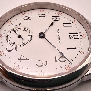May include: A close-up of a vintage Waltham watch with a white face, black hands, and a small subdial. The watch has a silver-colored case and a black leather band. The watch face features black Arabic numerals and the word "WALTHAM".