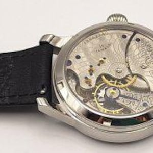 May include: A silver-toned wristwatch with a black leather band. The watch face reveals the intricate internal mechanisms. The band is secured with a silver buckle. The watch is a classic accessory.