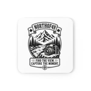 Puede incluir: Un posavasos cuadrado con un gráfico en blanco y negro de una cámara sobre un tocón de árbol frente a un paisaje de montaña y bosque. El texto dice NORTHOF49 arriba y FIND THE VIEW. CAPTURE THE MOMENT. abajo con una brújula.