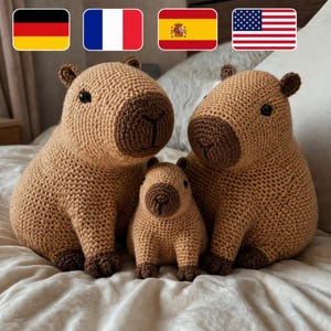 May include: Three crocheted capybaras in varying sizes, in shades of brown. The largest capybara is on the left, the smallest in the center, and a medium-sized one on the right. The capybaras have dark brown features and are sitting on a light-coloured surface.