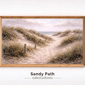Puede incluir: Una impresión enmarcada de un camino arenoso que conduce al océano, con hierbas altas y postes de madera con cuerda. La obra de arte está en tonos neutros, con el texto "Sandy Path - oakstudioes" en la parte inferior.