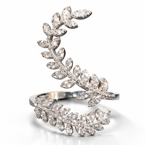 Op de afbeelding: Een zilverkleurige ring met een bladvorm, versierd met talrijke heldere, sprankelende edelstenen. Het ontwerp van de ring wikkelt zich om de vinger en creëert een elegante, door de natuur geïnspireerde esthetiek. De edelstenen zijn in een bladvormig patroon geplaatst.