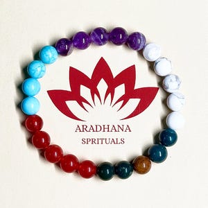 Könnte beinhalten: Ein Armband mit bunten Edelsteinperlen in Rot, Türkis, Lila und Weiß. Das Armband ist kreisförmig angeordnet. Der Text "ARADHANA SPRITUALS" ist rot unter einer roten Lotusblume abgebildet.