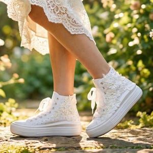 Può includere: Sneakers alte bianche con decorazioni floreali e suole platform. Le sneakers presentano delicati dettagli in pizzo e perle, con lacci bianchi annodati a fiocco. Scarpe per un'occasione speciale.