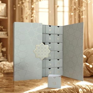 May include: A light gray advent calendar with a geometric star pattern on the doors and a central star-shaped clasp. The calendar features multiple small drawers labeled with numbers, including a detached drawer in the foreground marked with the number 13.