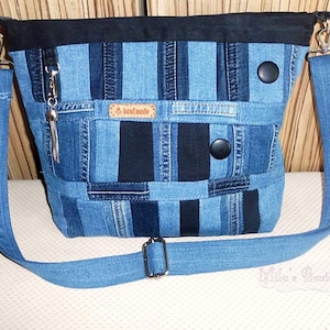May include: A patchwork denim crossbody bag with a black top and strap. The bag features a mix of blue denim patches, black accents, and silver hardware. It has a long, adjustable strap and a small tassel charm.