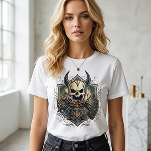 May include: White t-shirt with a cartoon illustration of a horned skull warrior, holding a sword and shield. The warrior is in blue, gold, and white, set against a blue and gold shield design.