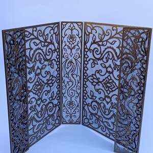 Könnte beinhalten: Ein vierflügeliger Paravent mit komplexen Laserschnitt-Designs in dunkler Bronzeoptik. Die Paneele zeigen detaillierte Muster aus geschwungenen Ranken, blühenden Rosen und stilisierten Drachenfiguren, die in die filigrane Struktur eingearbeitet sind.