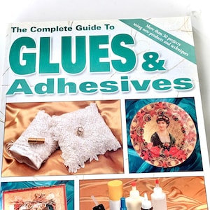 May include: A book titled "The Complete Guide to Glues & Adhesives" with a teal and white cover. The cover features images of craft projects, including decorative pillows and a vintage plate. The book promises more than 30 projects.