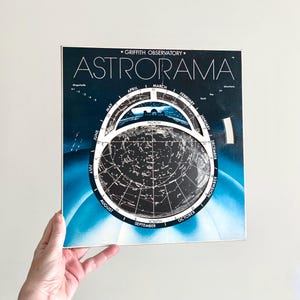 May include: A vintage "Astromara" star chart from the Griffith Observatory. The chart features a dark blue background with white star constellations and a rotating dial. The text includes months, directions, and the observatory name.