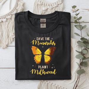 May include: Black t-shirt with a butterfly graphic and the text "Save the Monarchs Plant Milkweed" in yellow script. The butterfly design features yellow and brown wings. The shirt is a Gildan brand.