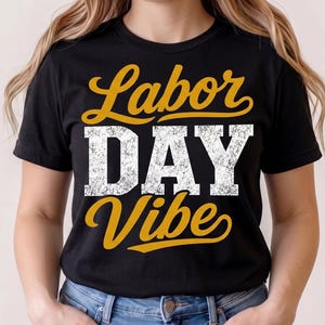 May include: A black short-sleeved t-shirt featuring the text Labor DAY Vibe printed on the front. The word Labor is in a yellow cursive script, DAY is in a large white distressed block font, and Vibe is in a yellow cursive script.