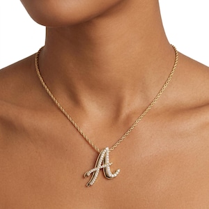 May include: A gold-toned rope chain necklace featuring a cursive letter A pendant. The pendant is crafted with a polished gold-toned metal finish and is embellished with a series of small, clear, sparkling stones set along the surface of the letter.