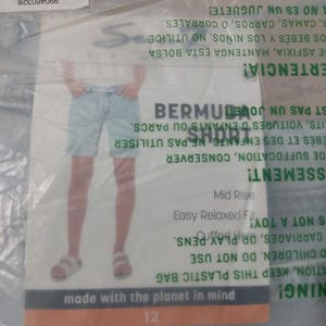 May include: Light blue denim Bermuda shorts in a clear plastic bag. The packaging features a product image, the text BERMUDA SHORT, Mid Rise, Easy Relaxed Fit, Cuffed Hem, and made with the planet in mind, along with a barcode and safety warnings.