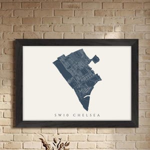 May include: Framed map print of the SW10 Chelsea area in a dark blue color. The map is set against a cream background and is enclosed in a black frame. The text "SW10 CHELSEA" is printed below the map.