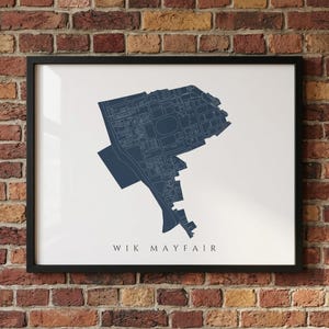 Może przedstawiać: Oprawiony wydruk mapy Wik Mayfair w kolorze granatowym. Mapa, z konturami ulic i kształtami budynków, znajduje się na białym tle. Wydruk jest w czarnej ramie i jest eksponowany na ceglanej ścianie.