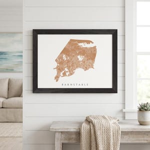 May include: Framed map print of Barnstable, Massachusetts, in a warm brown hue against a white background. The map is encased in a black wooden frame. The word "BARNSTABLE" is printed in a simple font below the map.