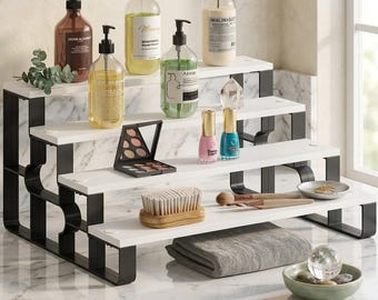 Peut inclure: Étagère à trois niveaux avec étagères blanches et supports noirs, contenant divers produits de beauté et de soins de la peau. Comprend des flacons avec distributeurs à pompe, du maquillage, du vernis à ongles et une brosse. Une serviette grise pliée et un bol décoratif sont également présents.