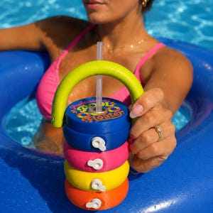 Puede incluir: Un portavasos flotante para piscina con el texto "Professor Cool Floater". El portavasos está hecho de secciones apiladas de colores brillantes: azul, rosa, amarillo y naranja. Tiene un asa verde y una pajita transparente.