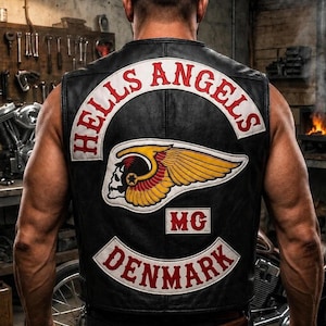 May include: A black leather waistcoat featuring a large embroidered patch on the back with the text HELLS ANGELS in a white arch, a central winged skull emblem in yellow and red, a small MG patch, and a bottom white arch patch reading DENMARK.