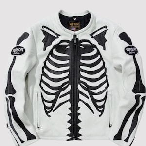 Könnte beinhalten: Weiße Lederjacke mit schwarzem Skelett-Design. Die Jacke hat einen durchgehenden Reißverschluss, zwei Vordertaschen und das Logo "Vanson Leathers" auf Brust und Arm. Das Skelett-Design umfasst Rippen und Armknochen.