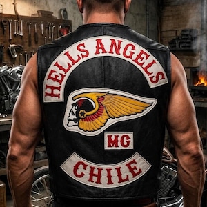 May include: A black leather waistcoat featuring a large embroidered patch on the back with the text HELLS ANGELS in red letters on a white curved background, a central winged skull emblem in yellow and red, the letters MG, and CHILE in red.