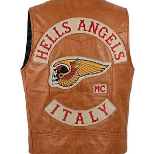 Może przedstawiać: Brązowa skórzana kamizelka z logo "Hells Angels" i naszywką "ITALY". Kamizelka posiada emblemat czaszki ze skrzydłami i naszywkę "MC". Kamizelka jest w klasycznym stylu motocyklowym.