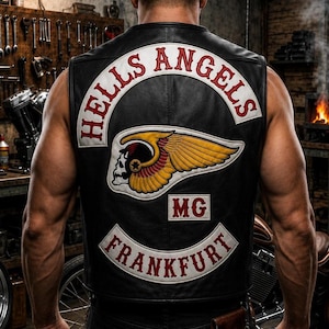 Może przedstawiać: Czarna skórzana kamizelka z dużą haftowaną naszywką na plecach, zawierającą napis HELLS ANGELS w białym łuku, centralny emblemat uskrzydlonej czaszki w kolorze żółtym i czerwonym, litery MG oraz dolną białą naszywkę z napisem FRANKFURT.