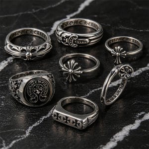 Könnte beinhalten: Eine Auswahl an Silberringen mit verschiedenen Designs, darunter Kreuzmotive, florale Muster und eingravierter Text. Die Ringe werden auf einer dunklen, strukturierten Oberfläche präsentiert, die ihre komplizierten Details und Handwerkskunst hervorhebt.