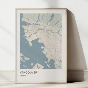 Può includere: Una stampa incorniciata di una mappa di Vancouver, Canada, caratterizzata da una tavolozza di colori tenui con acqua blu polveroso e masse terrestri beige. La mappa mostra strade e topografia, con il testo VANCOUVER CANADA stampato in basso.