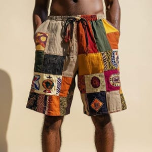 May include: Patchwork shorts with a drawstring waist. The shorts feature a variety of colourful fabric patches in shades of orange, yellow, green, and red. The shorts have pockets and a neutral-coloured waistband.